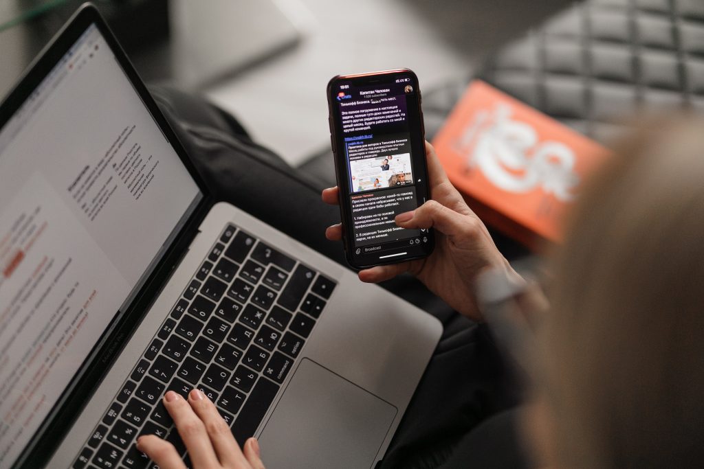 maxim-ilyahov-0aRycsfH57A-unsplash a person reading an email on a phone and typing on a laptop